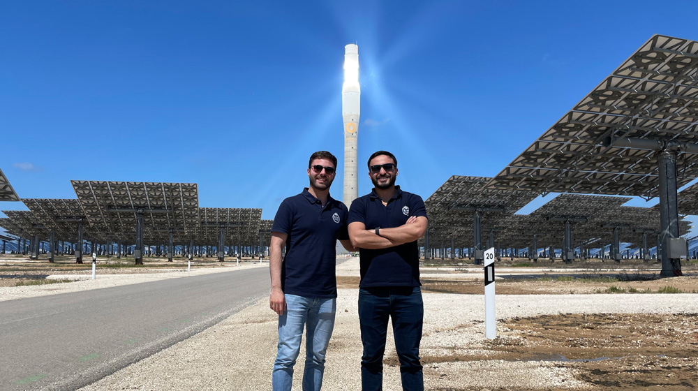 Two men standing at a large concentrated solar power plant, with mirrors surrounding them.